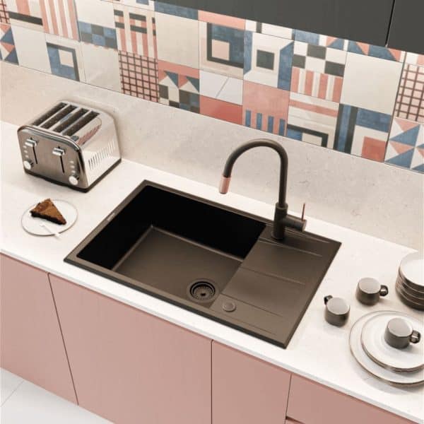 Sleek black kitchen sink with modern faucet, positioned on a white countertop with pastel pink cabinets, in a vibrant kitchen with geometric patterned backsplash.